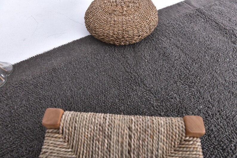 May include: A close-up of a gray, textured rug with a woven wicker stool and a woven wicker ottoman. The stool and ottoman are both in the center of the image.
