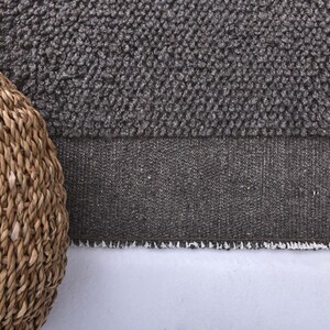 May include: A close-up of a brown woven basket with a gray and white textured rug underneath.