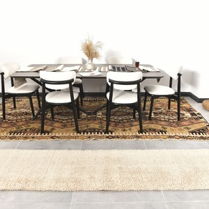 Puede incluir: Una alfombra de patr&oacute;n beige y marr&oacute;n con un corredor de alfombra de pelo blanco y beige delante de una mesa de comedor con seis sillas. La mesa tiene una tapa de madera oscura y patas de metal negro. Hay un jarr&oacute;n con flores secas sobre la mesa.