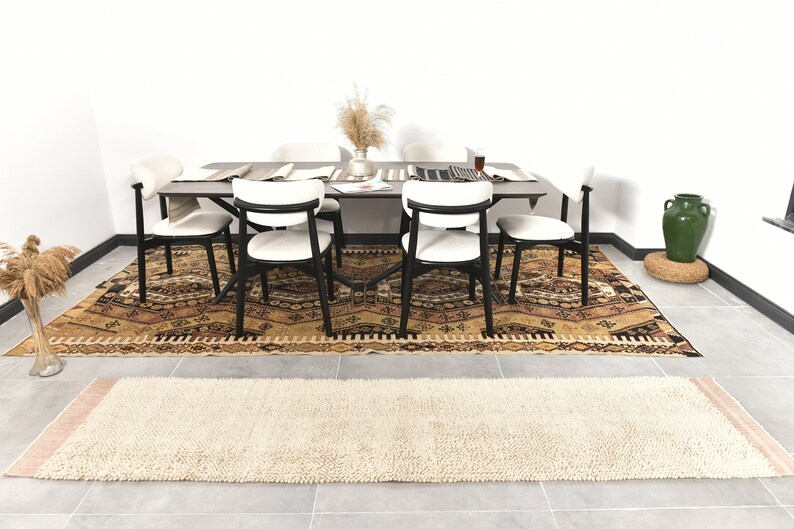 Puede incluir: Una alfombra de patr&oacute;n beige y marr&oacute;n con un corredor de alfombra de pelo blanco y beige delante de una mesa de comedor con seis sillas. La mesa tiene una tapa de madera oscura y patas de metal negro. Hay un jarr&oacute;n con flores secas sobre la mesa.