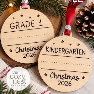 May include: Two circular wooden decorations featuring laser-cut star motifs and ribbons. One piece is engraved with GRADE 1, the other with KINDERGARTEN. Both include lines for writing and the text Christmas 2026. They are finished with pink and red ribbons.