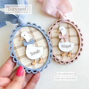 Può includere: Due ornamenti decorativi in legno a forma di oca con bordi smerlati. Uno è blu con un papillon blu e il nome "Jonah". L'altro è rosa con un fiocco rosa e il nome "Abigail". Entrambi hanno uno sfondo a quadri e sono legati con un nastro.