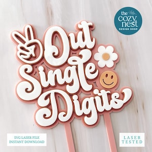 May include: A pink and white cake topper with the words "Out Single Digits" in a playful font. The design includes a peace sign, a daisy, and a smiling face. The text "SVG Laser File Instant Download" is also visible.