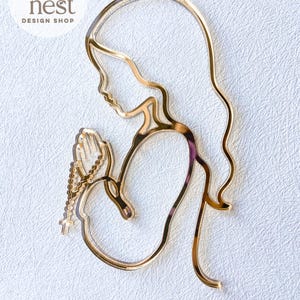 Può includere: Un design dorato tagliato al laser di una persona in preghiera, con un rosario. Il design è una silhouette con capelli fluenti e un contorno delicato. Il testo "SVG LASER FILE" è in basso.