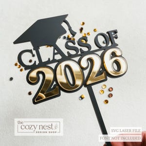 Könnte beinhalten: Schwarzer und goldener Tortenaufsatz zur Graduierung mit dem Text "CLASS OF 2026" und einer Abschlusskappe. Die Zahlen sind goldfarben, der Rest des Designs ist schwarz. Das Logo von The Cozy Nest Design Shop ist sichtbar.