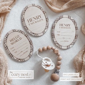 Op de afbeelding: Houten baby aankondigingsplaten met geruite randen, met de naam "HENRY EMERSON" en "HELLO WORLD". Bevat ruimte voor baby's details. Een houten fopspeenclip met een witte fopspeen is ook afgebeeld.