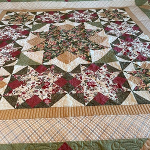 May include: A quilted bedspread with a floral pattern in shades of red, green, and beige. The quilt features diamond and star designs, with intricate stitching details. The overall design is a mix of floral and geometric patterns.