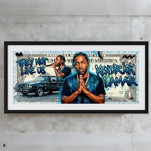 Op de afbeelding: Ingelijste kunstwerk met Kendrick Lamar in een dollarbiljetontwerp. Het kunstwerk bevat de tekst "THEY NOT LIKE US" en "Kendrick Lamar" in blauwe graffiti-stijl letters. Een zwarte auto is ook afgebeeld.