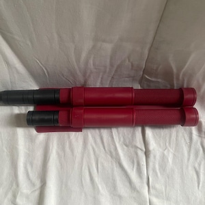 May include: Two red and black tools are displayed on a white surface. The tools have a cylindrical body with a textured grip and a black tip. One tool is larger than the other. The tools appear to be new.