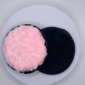 Può includere: Due dischetti tondi per struccarsi, uno rosa e uno nero, su una superficie bianca.