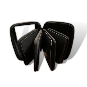 Könnte beinhalten: Schwarze CD/DVD-Aufbewahrungstasche, geöffnet, um die einzelnen Hüllen anzuzeigen. Die Tasche besteht aus einem strukturierten Material und hat einen Reißverschluss. Jede Hülle ist schwarz mit einem weißen Rand. Die Tasche ist für mehrere Discs konzipiert.