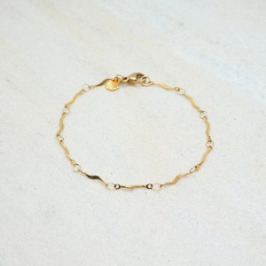 Puede incluir: Un brazalete de cadena dorada con un diseño ondulado. El brazalete tiene un cierre de langosta.