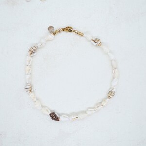 May include: A white seashell necklace with a gold clasp. The necklace is made of small, white seashells strung together on a thin cord.