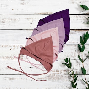 Peut inclure: Cinq chapeaux en tissu de différentes couleurs avec des liens. Les chapeaux sont empilés, la couleur la plus foncée en haut et la couleur la plus claire en bas. Les couleurs sont le violet, la lavande, le rose, le rose clair et le marron.