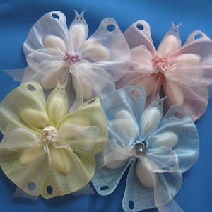 May include: Four decorative flower-shaped favors made of white tulle and fabric petals. The favors are in shades of light blue, light pink, light green, and white. Each favor has a small decorative flower in the center.