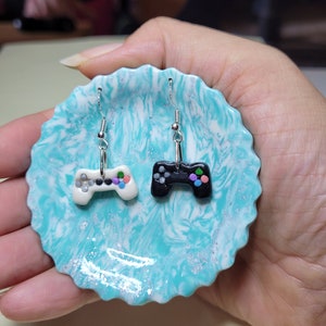 May include: A pair of silver earrings with a white and black video game controller charm. The controllers have colourful buttons.
