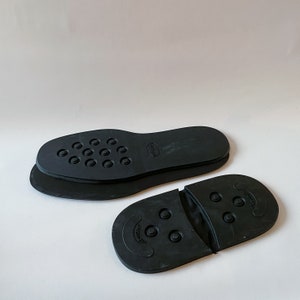 Puede incluir: Dos plantillas de zapatos negras con una superficie texturizada y pequeños puntos en relieve. La plantilla de la izquierda tiene la palabra "Ecco" impresa. La plantilla de la derecha tiene la palabra "Grip" impresa.