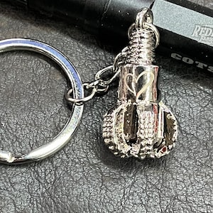 May include: Silver drill bit keychain with a heart engraved on the side. The keychain has a silver ring and a silver chain.