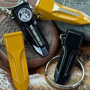 May include: Keyrings with a yellow and black design. One black keyring has the text "WE CAN DIG IT!" and a graphic. Another yellow keyring has the name "HAROLD". The keyrings are on a metal ring.