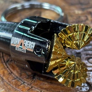 May include: A black and gold metal keychain with a drill bit design. The drill bit has two gold-coloured, fan-shaped cutting heads. The text "Worm Energy Services" is printed on the side.