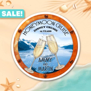 May include: A round orange and white sticker with a porthole design. The sticker says "Honeymoon Cruise Disney Cruise 15 Years" and features two champagne glasses clinking with a mountain range and a cruise ship in the background. The text "Ammy and Martin" is below the glasses.