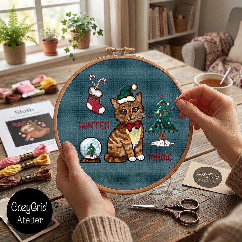 K&ouml;nnte beinhalten: Ein Kreuzstichprojekt in einem Holzrahmen auf dunkelblauem Stoff mit einer braunen getigerten Katze mit gr&uuml;ner Weihnachtsm&uuml;tze und roter Fliege, einem Weihnachtsstrumpf, einer Schneekugel und einem Tannenbaum mit dem Text WINTER MAGIC.