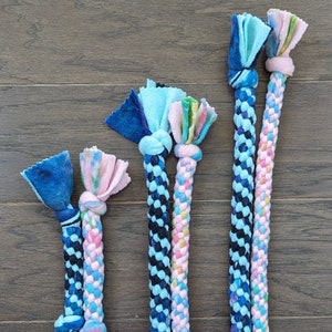 May include: Four colorful braided dog toys with knotted ends. The toys are made of soft fabric in shades of blue, pink, and green.
