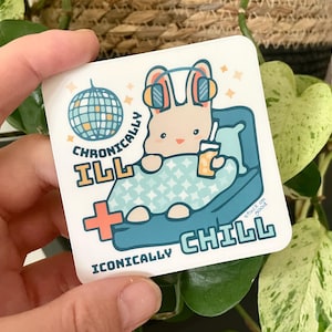 May include: Square sticker with a cartoon rabbit wearing headphones, relaxing on a blue couch and holding a drink. The sticker reads "Chronically Ill" and "Iconically Chill" with a disco ball graphic.
