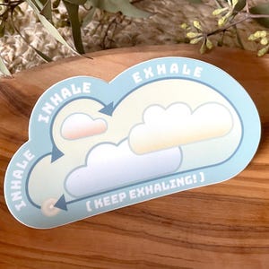 Könnte beinhalten: Ein blauer und weißer Aufkleber mit einem Wolkenmotiv und den Wörtern "inhale" und "exhale" in einem Kreis. Der Aufkleber enthält auch den Text "(keep exhaling!)".