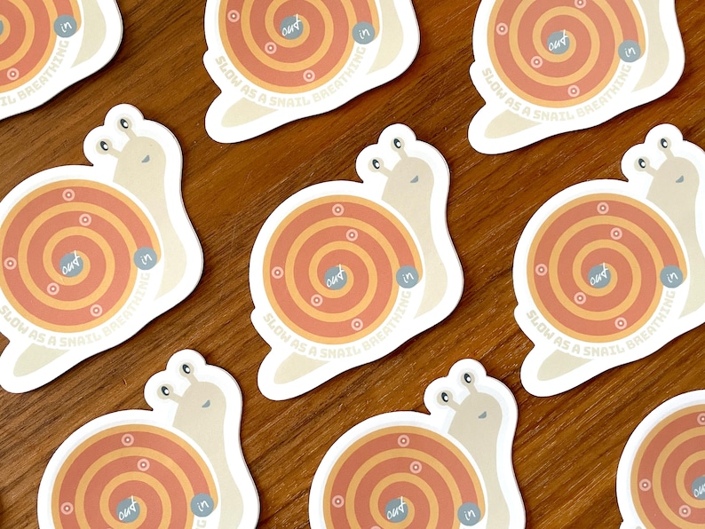 Puede incluir: Conjunto de nueve pegatinas en forma de caracol con un dise&ntilde;o en espiral de color naranja y amarillo. El texto "Slow as a snail, breathing in" est&aacute; impreso en cada pegatina.