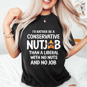May include: Black t-shirt with white text that reads "I'D RATHER BE A CONSERVATIVE NUTJOB THAN A LIBERAL WITH NO NUTS AND NO JOB." The word "NUTJOB" has a star with sunglasses in place of the "O".