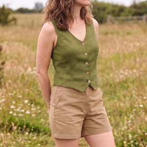 Pode incluir: Um colete sem mangas verde-oliva com decote em V e fecho frontal com cinco pequenos bot&otilde;es castanhos. O colete &eacute; combinado com cal&ccedil;&otilde;es de cor bege com cintura padr&atilde;o, bolsos laterais e uma bainha reta e simples.