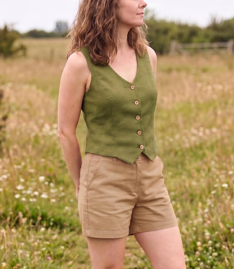 Pode incluir: Um colete sem mangas verde-oliva com decote em V e fecho frontal com cinco pequenos bot&otilde;es castanhos. O colete &eacute; combinado com cal&ccedil;&otilde;es de cor bege com cintura padr&atilde;o, bolsos laterais e uma bainha reta e simples.
