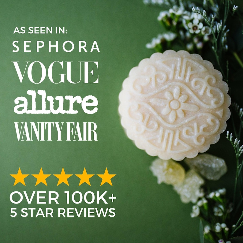 May include: A round, off-white soap bar with an embossed floral pattern. Text reads: AS SEEN IN: SEPHORA VOGUE allure VANITY FAIR. Five yellow stars are displayed above the text: OVER 100K+ 5 STAR REVIEWS. The soap is set against a dark green background.