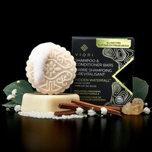 May include: A Viori Hidden Waterfall shampoo and conditioner bar set with a circular embossed bar featuring white foam, a rectangular base bar, wooden sticks, white flowers, and rice grains next to a black product box with gold text.