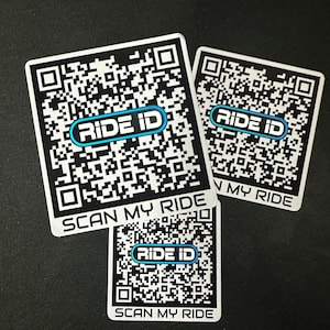 Pode incluir: Três autocolantes quadrados brancos com códigos QR pretos e o texto "RIDE ID" num oval azul. Os autocolantes também têm o texto "SCAN MY RIDE" na parte inferior. Os autocolantes estão numa superfície escura.