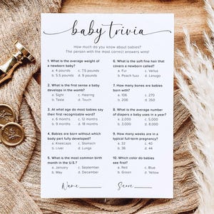 May include: A baby trivia game card with questions about newborns. The card has a minimalist design with the title "baby trivia" in elegant script. The card is on a wooden surface with decorative elements.