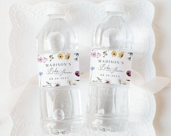 Può includere: Due bottiglie d'acqua in plastica trasparente con etichette bianche che presentano un motivo floreale e il testo "Madison's Baby Shower" e la data "08.20.20XX". Le bottiglie sono su un pizzo bianco.
