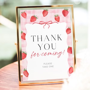 May include: A pink and white gingham background with red strawberries and a white sign that says "Thank You for coming! Please take one".