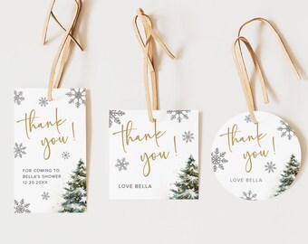 Op de afbeelding: Drie witte cadeaulabels met gouden tekst "thank you!". De labels hebben een winterthema met sneeuwvlokken en een illustratie van een kerstboom. Elk label is bevestigd aan een bruin lint.