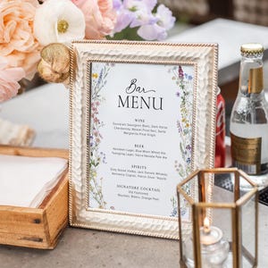 May include: A white framed bar menu with a floral design and the text "Bar Menu". The menu lists wine, beer, spirits, and a signature cocktail.