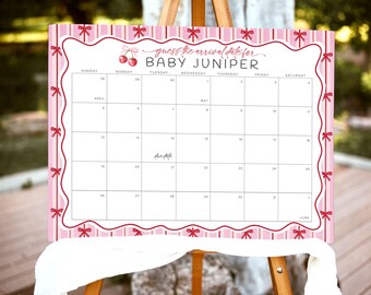 Puede incluir: Un calendario rosa y blanco sobre un caballete de madera, diseñado para un baby shower. El calendario está decorado con lazos y el texto "guess the arrival date for BABY JUNIPER". El calendario incluye fechas de abril, mayo y junio.