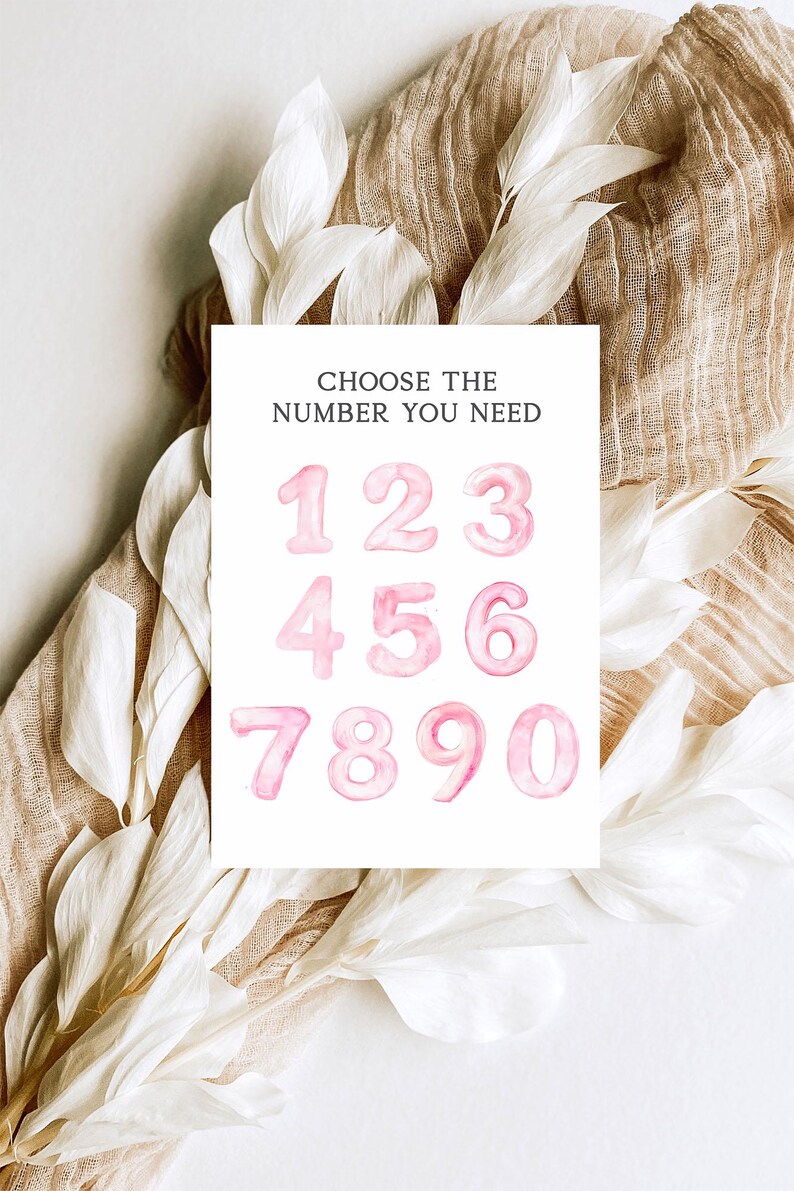 May include: A white card with the text "CHOOSE THE NUMBER YOU NEED" above pink watercolor numbers 1 through 0. The card is surrounded by white floral accents and a tan fabric.