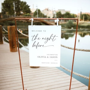 K&ouml;nnte beinhalten: Ein wei&szlig;es Schild mit schwarzem Text, auf dem steht "Willkommen zur Nacht vor der Feier von Olivia & Jason am 10. August 20XX in Oak Glen, CA". Das Schild h&auml;ngt an einem Gestell aus Kupferrohren.