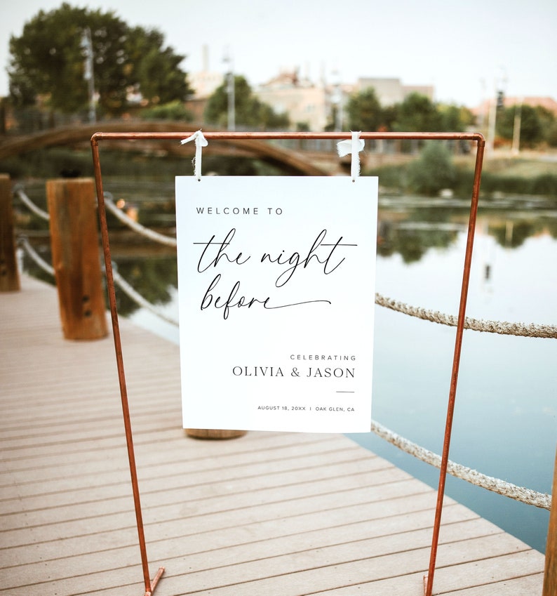 K&ouml;nnte beinhalten: Ein wei&szlig;es Schild mit schwarzem Text, auf dem steht "Willkommen zur Nacht vor der Feier von Olivia & Jason am 10. August 20XX in Oak Glen, CA". Das Schild h&auml;ngt an einem Gestell aus Kupferrohren.