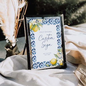 May include: A printable sign with a blue and white tile pattern border and a lemon and flower illustration. The sign says "Fully Editable Custom Sign Add Your Own Text Here".