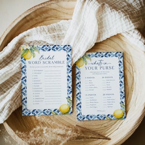 May include: Two printable bridal shower game cards with a blue and white tile pattern and lemons. The first card is a word scramble game with the title "Bridal Word Scramble". The second card is a "What's in Your Purse" game with a list of items and points.