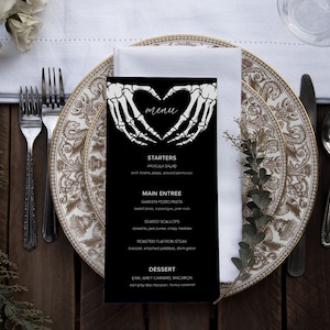 May include: A black and white menu with a skeleton hand heart design. The menu lists starters, main entree, and dessert options. The text reads: "menu", "Starters", "Arugula Salad", "Main Entree", "Garden Pesto Pasta", "Seared Scallops", "Roasted Flatiron Steak", "Dessert", "Earl Grey Caramel Macaron".