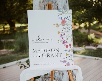 Op de afbeelding: Een wit welkomsbord voor een bruiloft met een bloemenontwerp. Het bord staat "Welkom op de bruiloft van Madison en Grant 08.28.20XX | Proctorville, VT".