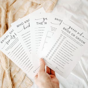 Puede incluir: Una mano sosteniendo una pila de hojas de juego blancas para la despedida de soltera. Las hojas tienen texto negro con títulos como "Bridal Shower Family", "Who Knows the Bride" y "Guess Who Bride or Groom". El fondo es una tela beige claro.